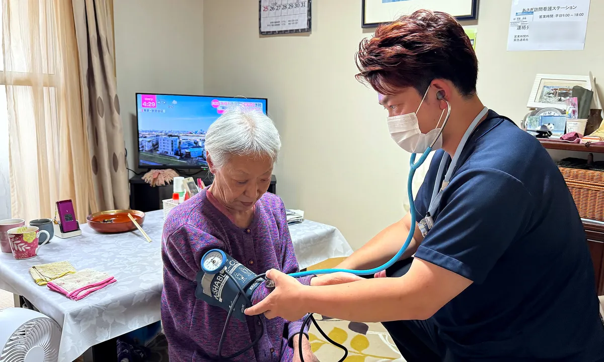 自宅の居間で利用者さまの血圧を測る看護師